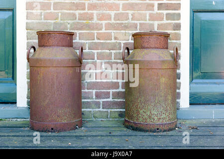 two old rusted churns with old wall with stones as background between tow green doors Stock Photo