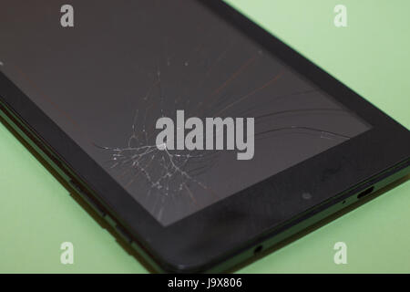 Black smartphone with a broken display on a light green background. Stock Photo