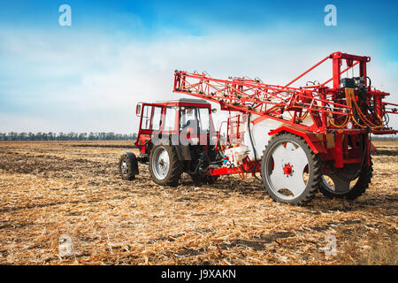 Red tractor with trailed sprayer in a field against a blue sky in a sunny day. Stock Photo