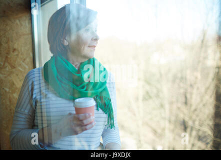Serene female with glass of drink looking through window Stock Photo