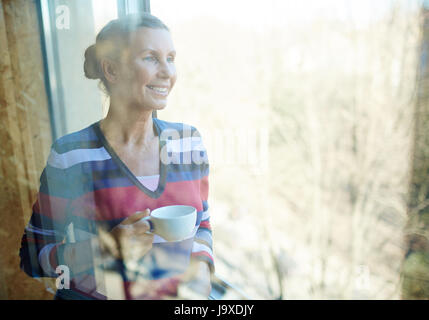 Calm woman with cup of tea enjoying sunny day by the window Stock Photo
