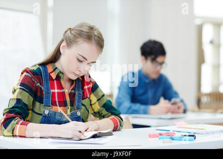 Diligent learner writing lecture by desk in college Stock Photo