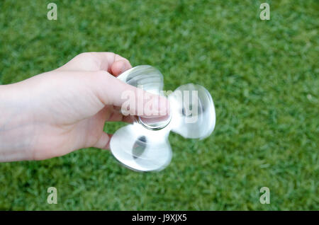 A childs hand holding a spinning silver fidget spinner against a green background Stock Photo