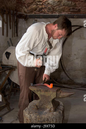 Traditionally dressed Farrier creating horseshoes from raw iron using a hammer and anvil, Wales, UK Stock Photo