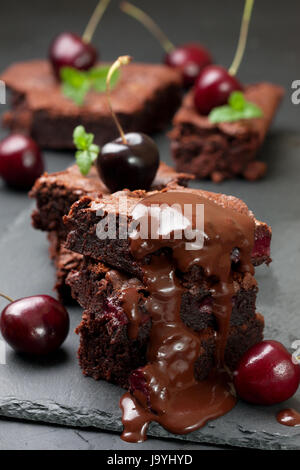 few pieces of brownie with cherries and with chocolate cream on a black concrete background Stock Photo