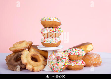 Cake donuts with white frosting and colorful sprinkles stacked on and around a small pedestal surrounded by birthday presents. Number 1 candle burning Stock Photo