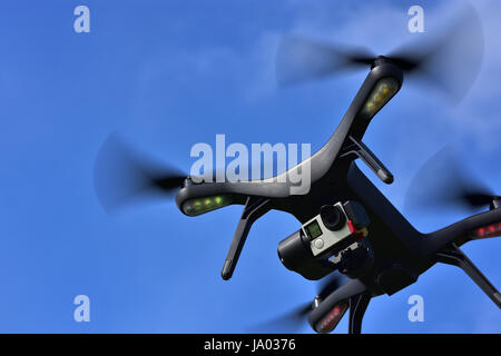 Black drone with camera flying over blue sky. Angle view, copy space. Stock Photo