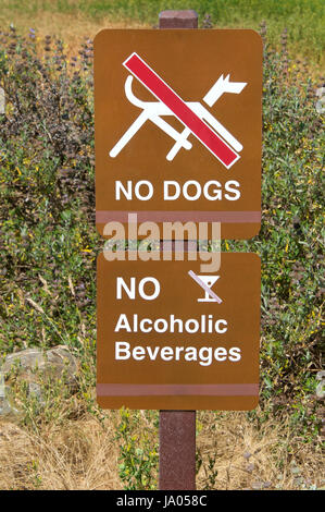Brown signs, no dogs and no alcoholic beverages. Tall weeds growing in background. Stock Photo