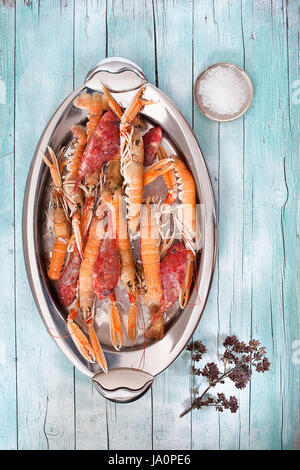 Oval plate with fresh raw lobsters and scorpionfish on wood background, with coarse salt and thyme flowers, top view shot. Stock Photo