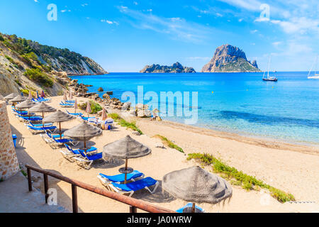 View of Cala d'Hort beach with sunbeds and umbrellas and beautiful azure blue sea water, Ibiza island, Spain Stock Photo