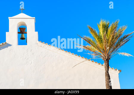 White church tower and palm tree with blue sky in background in Sant Vicent de sa Cala village in northern part of of Ibiza island, Spain Stock Photo