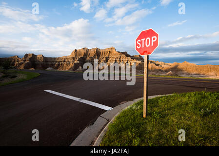 A stop sign at an intersection in Badlands National Park, South Dakota. A rock formation can be seen in the background. Stock Photo