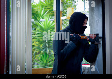 Burglar with crowbar trying break the window to enter the house Stock Photo