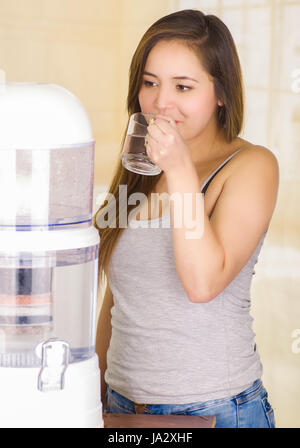 Beautiful woman drinking a glass of water with a filter system of water purifier on a kitchen background Stock Photo