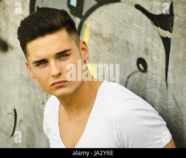 Handsome young man leaning against urban graffiti covered wall Stock Photo