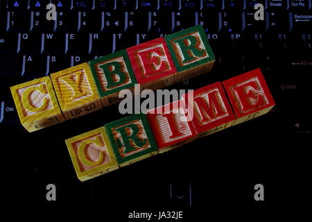 The term cyber crime displayed visually on a shadowy dark computer keyboard using colorful wooden blocks Stock Photo