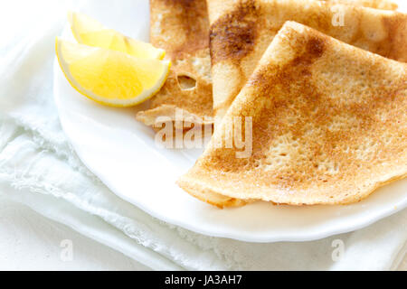 Crepes Suzette with lemon on white plate over white background, copy space. Delicious homemade Crepes for breakfast. Stock Photo