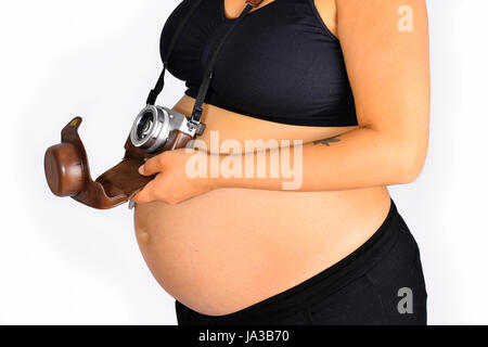 An analog camera with a brown leather casing hanging from a woman's neck by a strap and resting on her pregnancy bump. Stock Photo