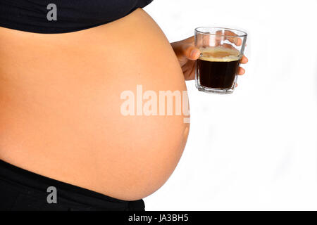 A close up of a pregnant woman's bump as she holds a glass off coffee in front of it. Stock Photo