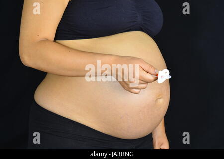 A pregnant woman holding out a pacifier in front of her tummy. Stock Photo