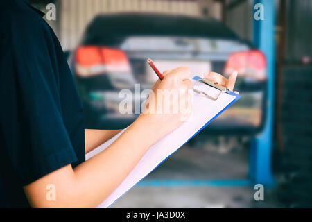 Portrait of smiling young female mechanic inspecting on a car in auto repair shop Stock Photo