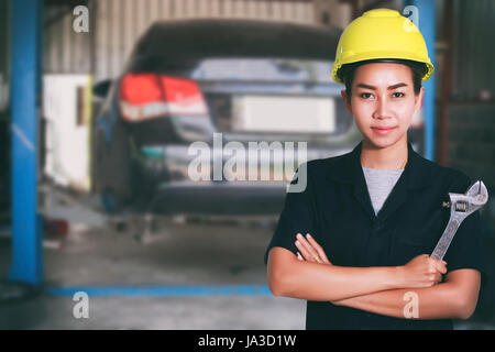 Portrait of smiling young female mechanic inspecting on a car in auto repair shop Stock Photo