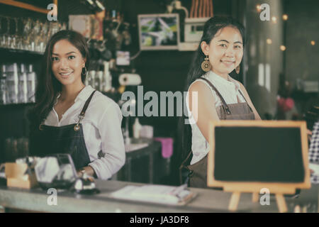 Two Asian women Barista smiling and using coffee machine in coffee shop counter Stock Photo