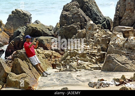 Tourist taking photos using smartphone of the rocky, rugged, spiky and sculpture type coastline at Arambol beach in Goa, India Stock Photo