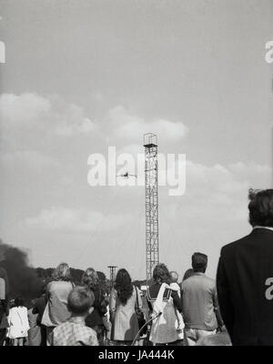 1970s, England, crowd watch as a man dives off a high steel tower at a funfair. Stock Photo