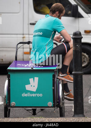 A Deliveroo cargo bike food delivery courier takes a break between deliveries in central London Stock Photo