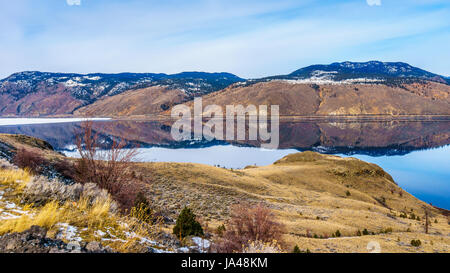 Kamloops Lake in BC, Canada, is a very wide portion of the Thompson River, on a cold winter day with the surrounding mountain reflecting in the water Stock Photo