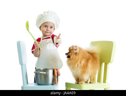 Kid boy playing chef with dog. Child weared cook feeds Spitz puppy. Stock Photo