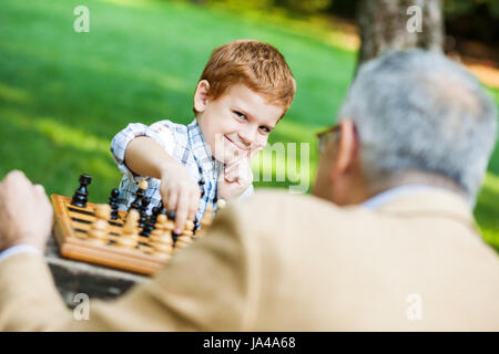 Grandfather and grandson are playing chess in park Stock Photo