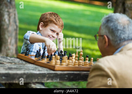 Grandfather and grandson are playing chess in park Stock Photo
