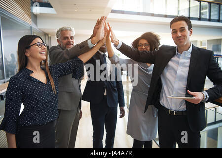 Cheerful office workers cooperating and giving high five standing and looking at camera together. Stock Photo