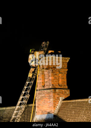 Floodlit fireman on ladder following night-time house chimney fire Stock Photo