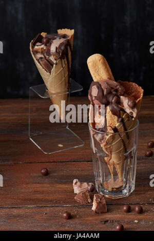 Ice cream in waffle cone in a glass and on a stand with a tasty ice cream , biscuits chocolate sweets and topping on a wooden brown background Stock Photo