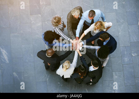 From above black and white coworkers having teambuilding in hall of office standing with hands stacked.