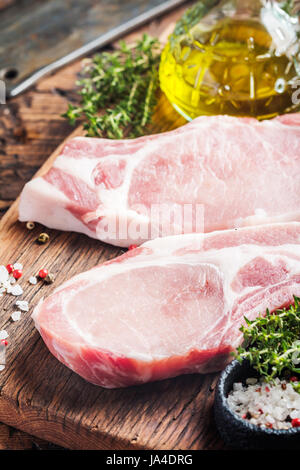 Raw pork meat chopes with herbs, oil and spices on wooden background. Stock Photo