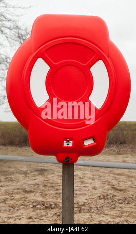 Bright red lifebuoy case on wooden pole stands on the beach Stock Photo