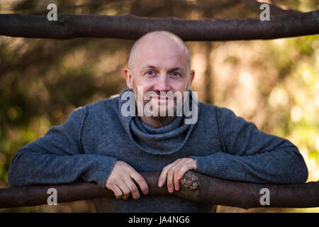 A brutal bald man in a sweater sits and rests on the nature Stock Photo