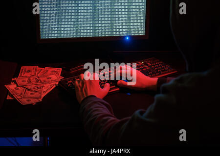 The man in the hood checks the malicious code on the keyboard. Cybercrime through the Internet. Stock Photo