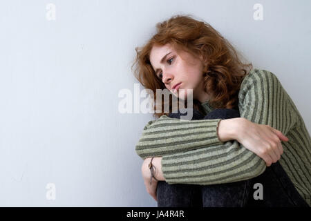 A beautiful red-haired girl leaned wearily against the wall and looked sadly away. She clasped her arms Stock Photo