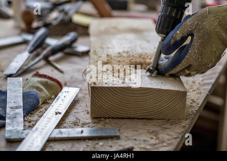 The carpenter makes holes with a drill in a wooden part Stock Photo