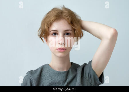 Red-haired girl holding hair in hands. She is dressed in a gray dress Stock Photo