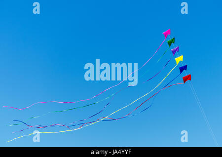 Rainbow colored kites flying against a beautiful blue sky Stock Photo