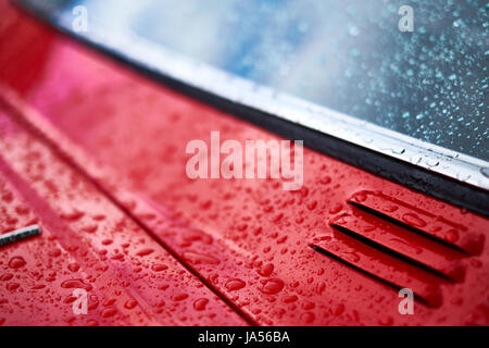 Rain falls on a red car forming water drops, close up of vent and window. Stock Photo