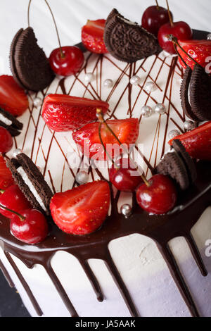 Mousse cake with fresh strawberries and cherries, decorated with biscuits and chocolate close-up. vertical