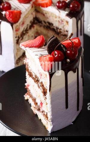 Slice of cake with fresh strawberries and cherries and chocolate close-up on a plate. vertical
