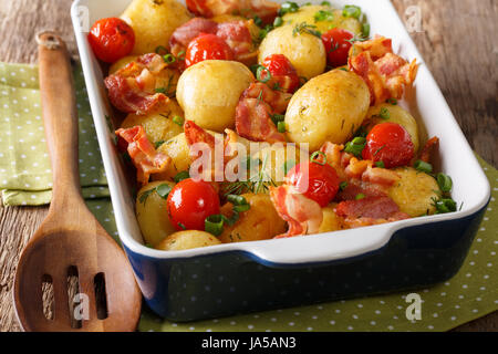 Delicious new potatoes baked with bacon, herbs and tomatoes close-up in a baking dish. horizontal Stock Photo